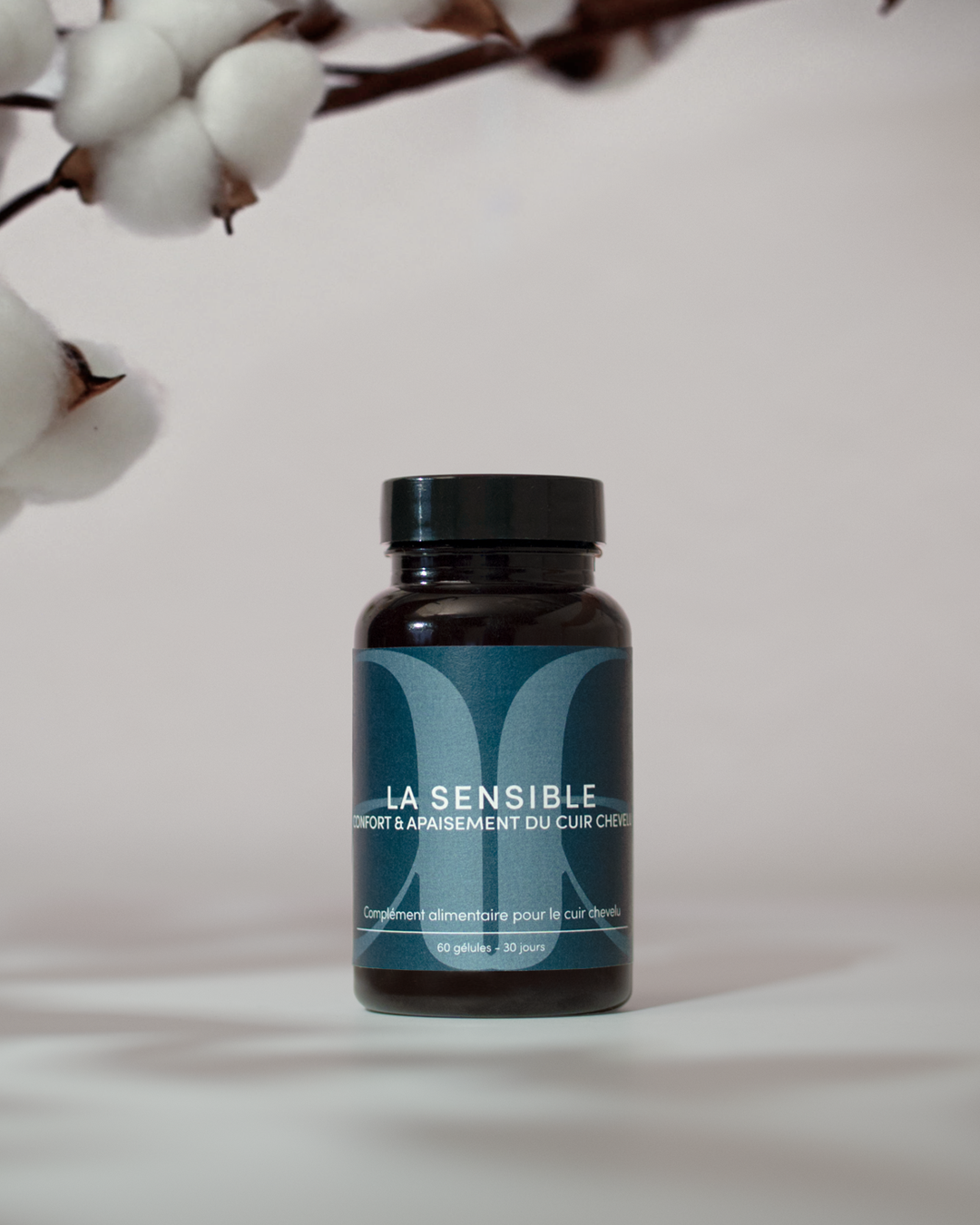 Présentation de la cure de compléments alimentaires capillaires "la sensible" KAAMI qui a pour objectif d'apaiser le cuir chevelu. Packaging bleu sur fond neutre