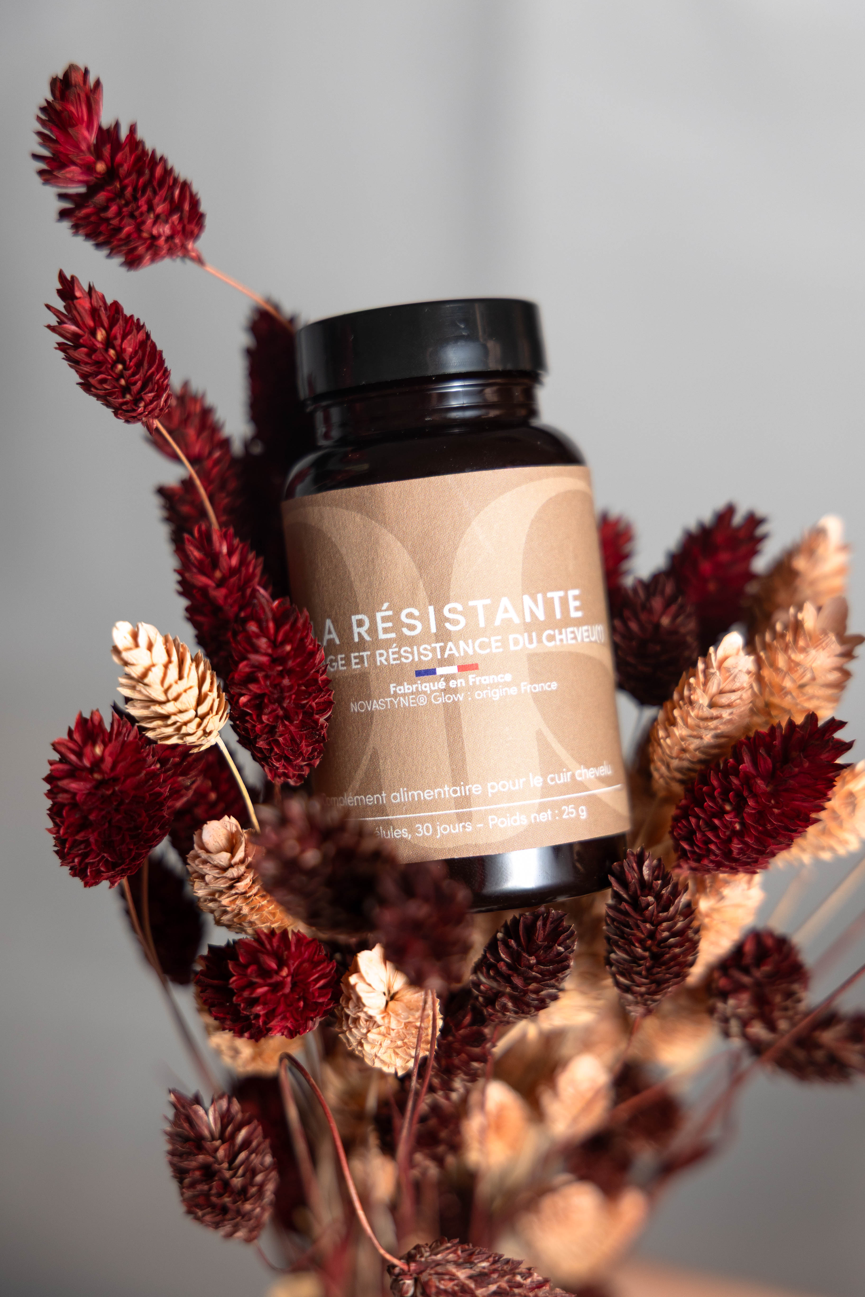pilulier noir, étiquette marron avec écrit La Rsistante. Complément alimentaire positionné sur un bouquet de fleurs séchées.