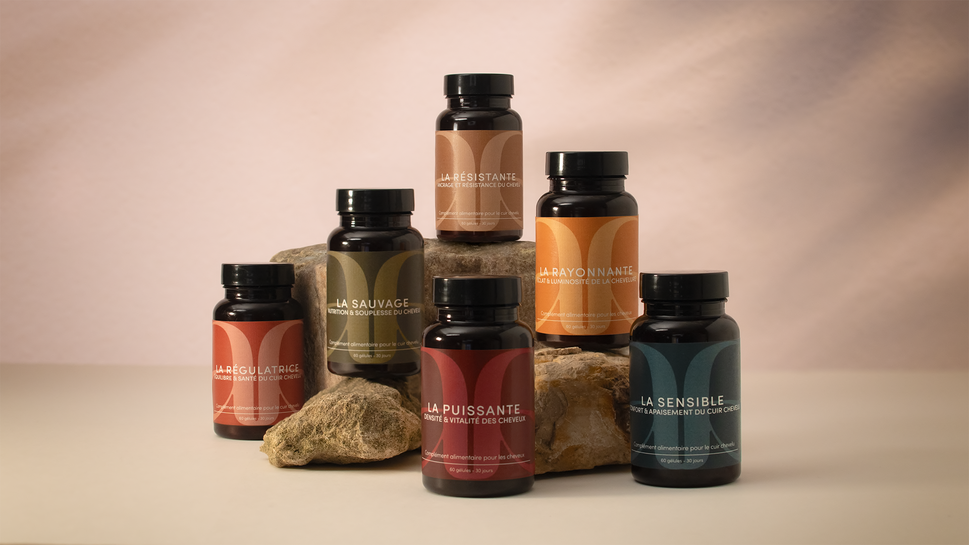 Présentation d'une gamme de 6 Produits de compléments alimentaires capillaires. Tous positionnées sur des cailloux avec un fond neutre
